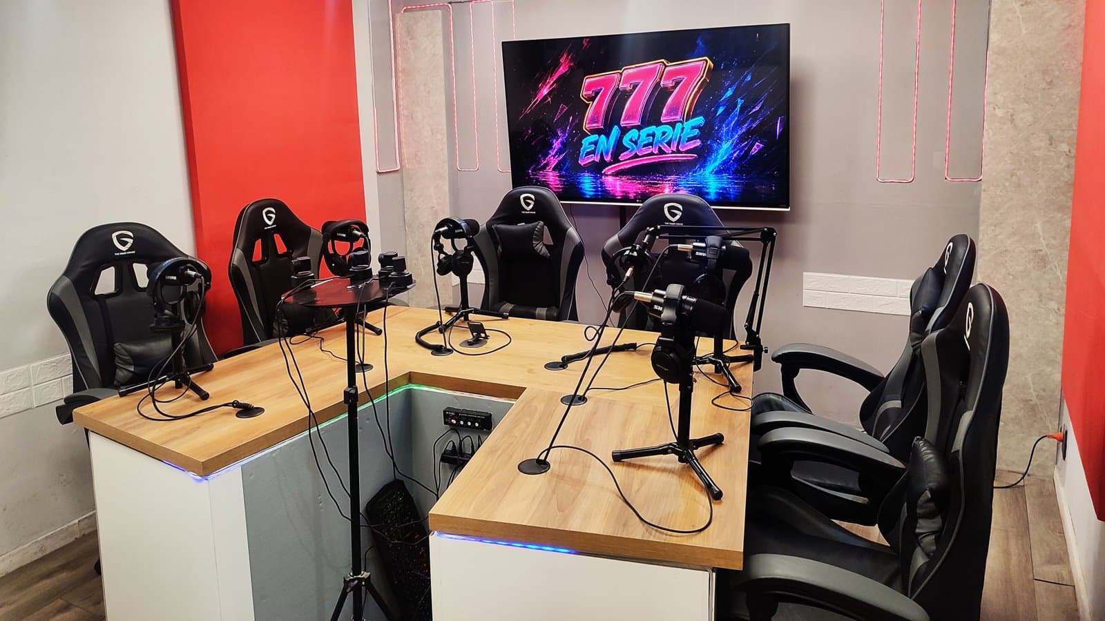 La mesa del estudio vista de frente, con cuatro puestos de micrófono y la pantalla del canal detrás